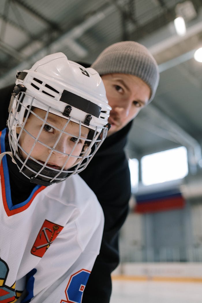A father and son bond while practicing ice hockey at an indoor rink.